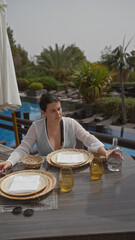 A young woman dining alone at a luxurious resort terrace in bali, contemplating a tranquil outdoor...