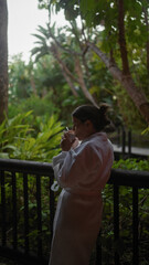 Fototapeta premium A young woman enjoys a peaceful moment with a cup of coffee on a lush balinese resort terrace.
