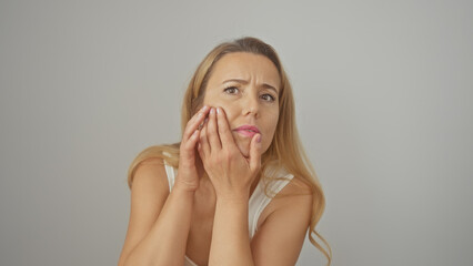 A worried young woman examines her face against a plain white background, expressing concern over beauty and aging.