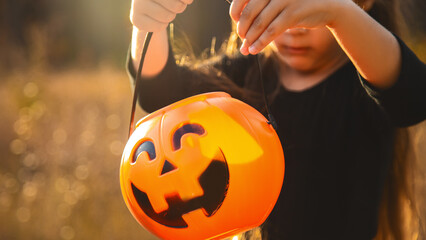 Close-up portrait of a 4-5 year old girl in a witch costume with a candy bucket against a...