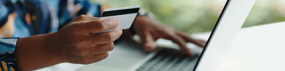 Close-up of person holding credit card while making online payment on laptop computer showing fingers typing on keyboard