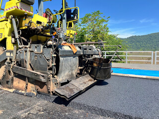 asphalt paver machine laying fresh asphalt on a road. The image captures the machinery in action, showing the spreader screed and other components, smooth layer of asphalt, construction site, civil