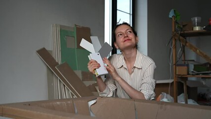 Woman smiling and contemplating paint color samples for a home renovation project. Tools and materials on shelves in the background
