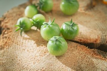 Green cherry tomatoes on wooden stump in bright rays of sun..