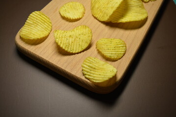 Fast food, not healthy food for human health. Thin slices of potatoes, corrugated chips are located on a light wooden background.