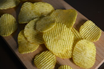 Fast food, not healthy food for human health. Thin slices of potatoes, corrugated chips are located on a light wooden background.