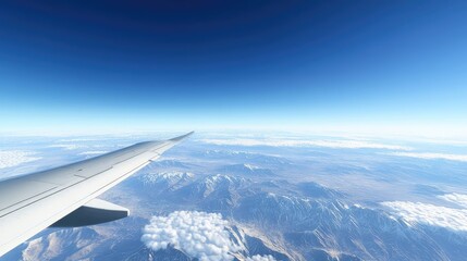 Obraz premium A beautiful blue sky with distant mountains visible below through an airplane window, with light clouds drifting across the horizon