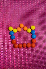 Food, sweets, bright colored round candies with chocolate filling are arranged on a glossy pink background with a graphic reflection.