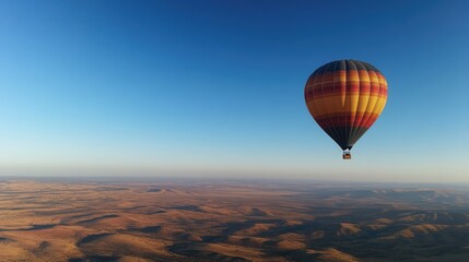 Obraz premium A clear blue sky with a colorful hot air balloon soaring high above a vast landscape, with the horizon stretching far in the distance