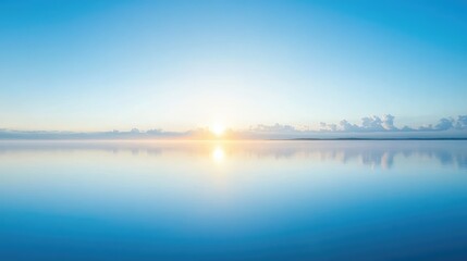 Fototapeta premium A clear sky over a calm lake at sunrise, with bright blue tones mirrored on the glass-like surface of the water