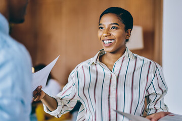 Happy ethnic woman listening colleagues with interest during working with reports in office