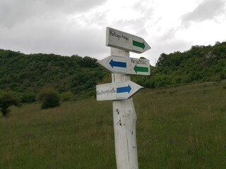 Blue and green arrow shaped hiking trail signs painted on a white wooden post