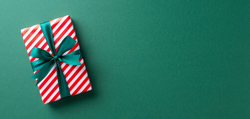 A beautifully wrapped Christmas gift box with red and white stripes and a green ribbon, placed on a green background, creating a festive holiday atmosphere