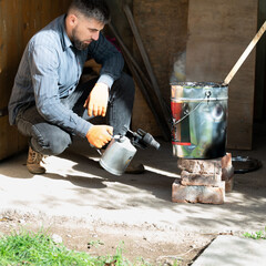 A man uses a kerosene lamp to heat resin in a bucket, working with waterproofing and resin.