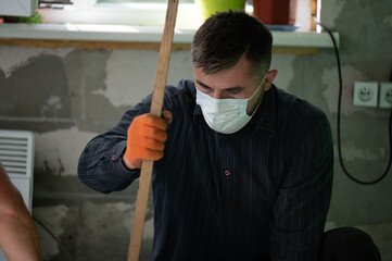 A man in a mask performs repair work on the background of a block wall.