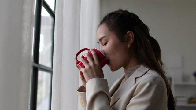 Business woman relaxing and standing by the window drinking coffee in the office.