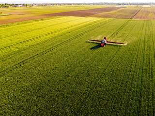 Drone shot of a tractor with sprayer in action on a vibrant green wheat farmland