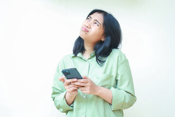 portrait of unhappy asian woman wearing over size green clothes looking above showing sad gloomy face expression confused using smartphone apps and online shopping isolated on white background