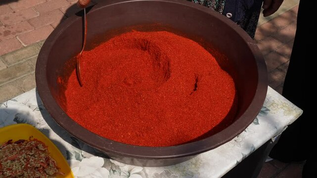 The manufacturer mixes the ground chilli with a wooden spoon.
