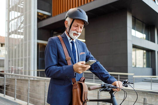Confident senior man pushing his bicycle and texting over smart phone while commuting to work in city