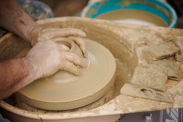 Man potter working on potters wheel making ceramic pot from clay in pottery workshop. 