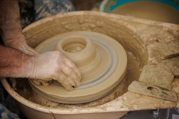 Man potter working on potters wheel making ceramic pot from clay in pottery workshop. 