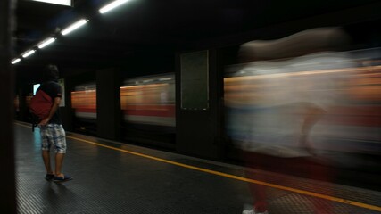 A lone traveler waits on a dark subway platform as a train rushes past during evening hours in a bustling urban environment