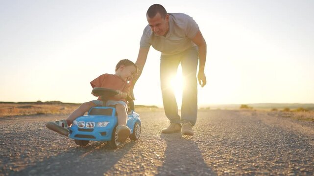 Father teaches his son how to drive a car. Family boy together concept. Father and child play with a toy car on the asphalt. Father takes his son for a ride in a toy car on the asphalt - lifestyle.