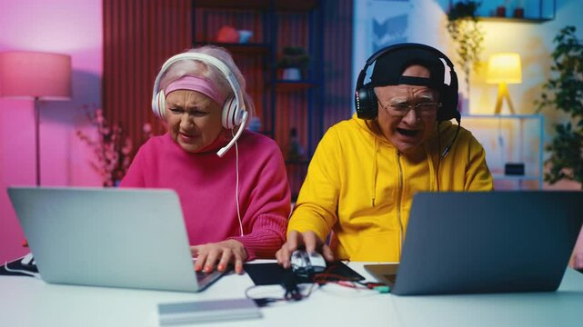 Modern seniors playing multiplayer game on laptops, woman losing competition