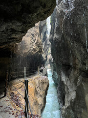 A narrow walkway winds through the rock cliffs at the valley's base alongside a flowing stream at Partnachklamm Gorge, Garmisch-Partenkirchen, offering a stunning alpine experience.