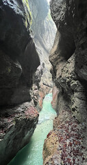 The beautiful stream flows through the rocky valley of Partnachklamm Gorge, where lush moss clings to stones, creating a vibrant and serene natural scene in Garmisch-Partenkirchen.