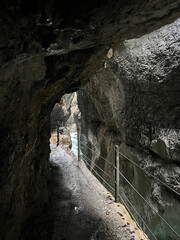 A narrow walkway winds through the rock cliffs at the valley's base alongside a flowing stream at Partnachklamm Gorge, Garmisch-Partenkirchen, offering a stunning alpine experience.