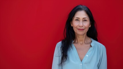 Fototapeta premium Professional Woman in Pastel Blue Blouse with Warm Smile Against Deep Red Background
