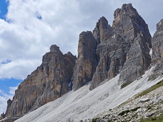 Close-up view of rugged rocky mountain cliffs with stratified formations under cloudy sky in alpine landscape. Geology and natural formation concept
