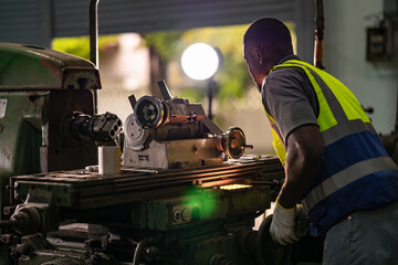 A focused technician operates heavy machinery in an industrial workshop. Dressed in a high-visibility vest, he exemplifies concentration and skill in a metalworking environment, ensuring precision.