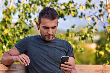 Fototapeta premium Young man using smartphone while relaxing on bench in park