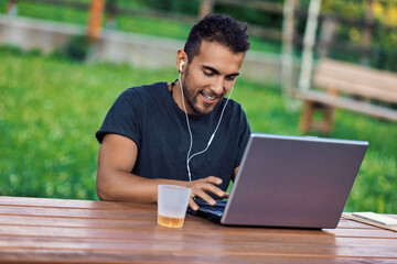 Fototapeta premium Freelancer working remotely outdoors on laptop and listening mus