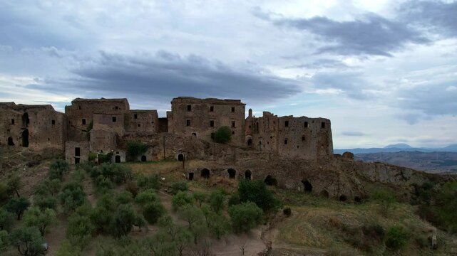 4K Aerial drone video of mystical ghost town on top of the hill with ruins and empty houses. Haunted village with crumbling structures and fallen church. Abandoned city Craco, Matera, Italy