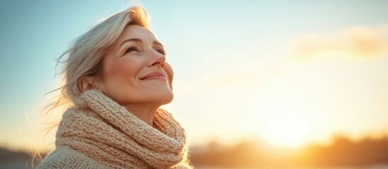 Portrait of a beautiful and happy mature woman in a warm jumper enjoying the winter sun set against a blue sky with copy space