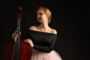 Beautiful young woman with cello on black background, space for text