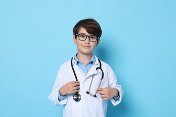 Fototapeta premium Boy with stethoscope pretending to be doctor on light blue background. Dreaming of future profession