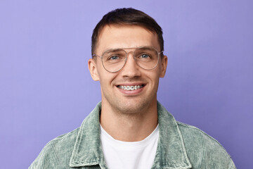 Fototapeta premium Smiling man with dental braces on violet background