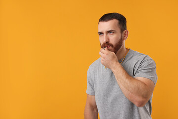 Young man blowing whistle on orange background, space for text
