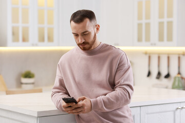 Handsome man looking at smartphone in kitchen