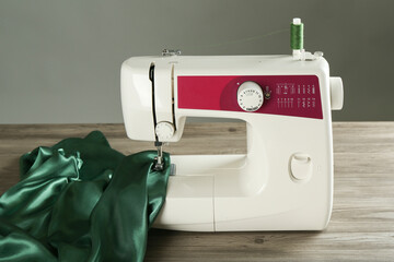 Sewing machine with green fabric on wooden table against gray background
