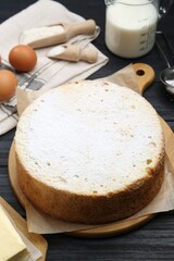 Delicious sponge cake and ingredients on black wooden table