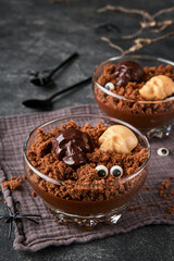 Halloween party chocolate puddings or Panna Cotta with brownie crumbles and chocolate sculls served in clear glass on grey dark background. Party idea for Halloween.
