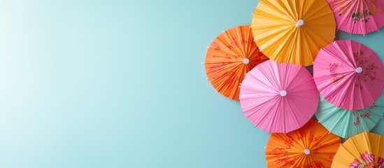 A set of multi colored cocktail drink umbrellas or paper parasols in vibrant pink and orange featuring floral designs against a light blue backdrop. with copy space image