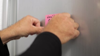 Businessman Placing Pink Sticky Note With Handwritten Motivational Message on Metallic Surface, Dont Forget To Smile, Fostering Positivity and Inspiration in Professional Office Setting