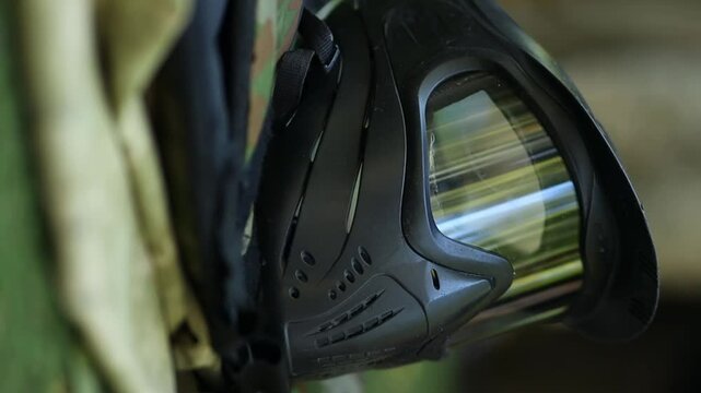 Paintball protective mask, Paintball battle, Game equipment. Black paintball mask, on the artificial playing field, Before the game. Paintball mask, vertical video